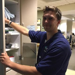 This is a picture of a student in front of an open cabinet. He is smiling and removing medical supplies before treating a patient.