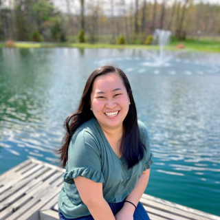 Person smiling sitting on bench in front of water with fountain