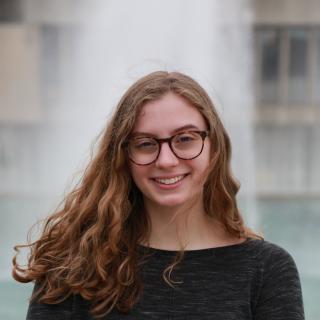 Person smiling wearing glasses standing in front of fountains