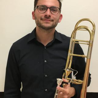 Person standing in black dress clothes holding trombone