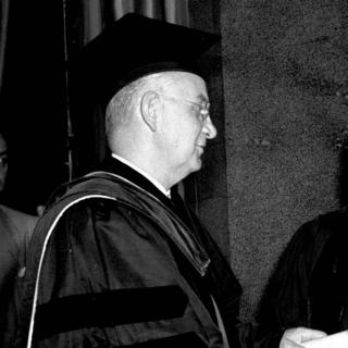 Black and white photo; in academic cap and gown.