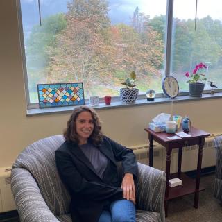 white woman sitting in a striped chair. fall leaves in the background along with plants and window art