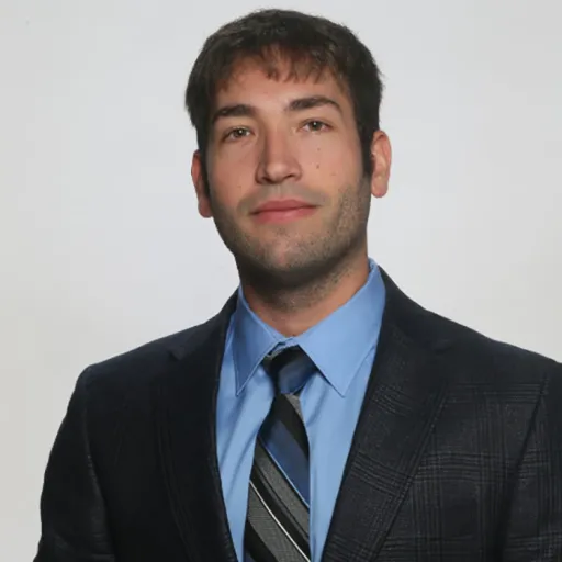 Head shot image of Dan DeCaria on white background. He is wearing a blue patterned suit coat over a light blue dress shirt and blue and grey patterned tie.
