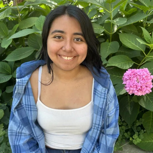 person sitting in front of green bush smiling