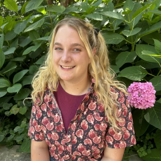 person sitting in front of green bush smiling
