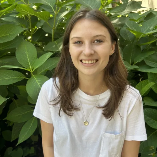 person sitting in front of green bush smiling