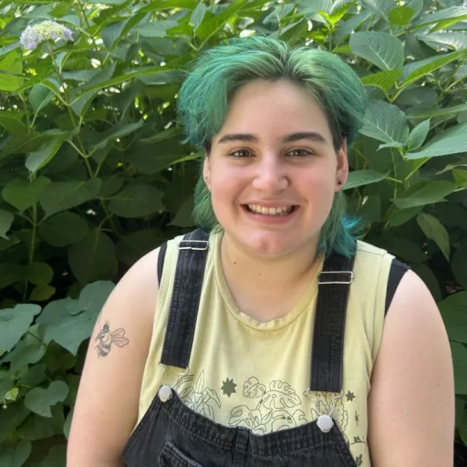 person sitting in front of green bush smiling