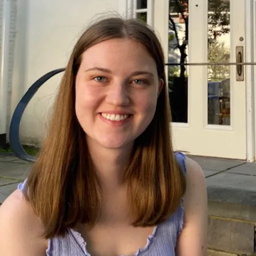 Photo of a woman's face with long hair standing in front of a building
