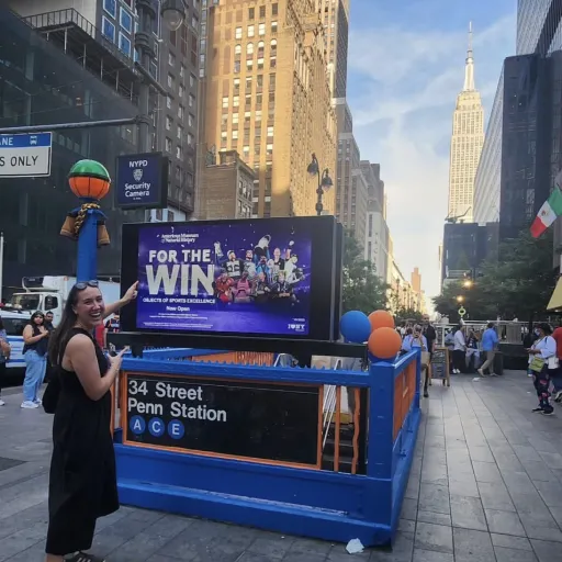 Maya Rodgers '20 points to a "For the Win" ad above the 34 Street Penn Station subway entrance, with the Empire State Building in the background.