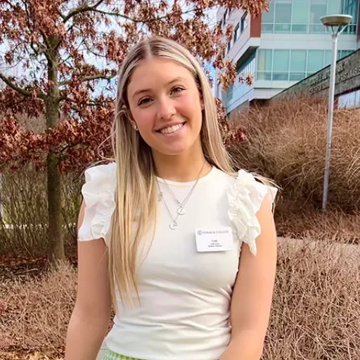 Woman with long hair standing outside in front of trees and buildings