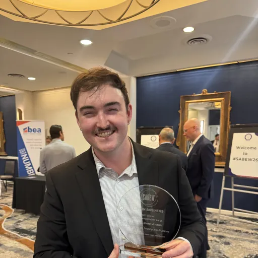 Peter Champelli smiles and holds a glass SABEW Best in Business award at an awards event.
